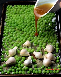 someone is pouring sauce on peas and garlic in a baking pan with other food items