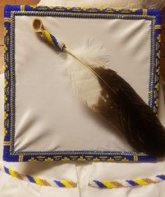 a feather is laying on top of a pillow with beaded trim around the edge