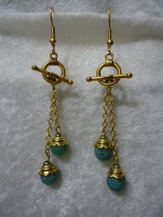 two pairs of gold tone earrings with turquoise beads hanging from chains on a white cloth