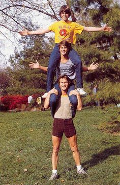 three people are standing on top of each other in the grass with their arms outstretched