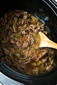 a slow cooker filled with beef and green peppers is being stirred by a wooden spoon