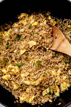 an egg fried rice dish in a black pan with a wooden spoon on the side