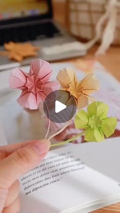 someone is holding origami flowers over an open book