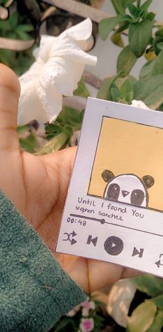 a person holding up a card with a panda on it in front of some flowers