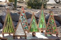 four small stained glass christmas trees sitting on top of a wooden stand in front of some rocks