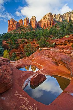 the red rocks are reflected in the small pool of water at the base of the mountain