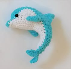 a crocheted blue and white dolphin is laying on its side with it's mouth open