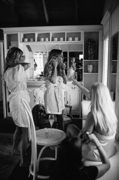 three women in white robes are brushing their teeth and looking into the mirror while another woman is sitting at a table