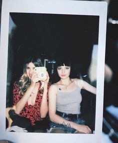 two young women sitting next to each other holding up a polaroid camera in front of them