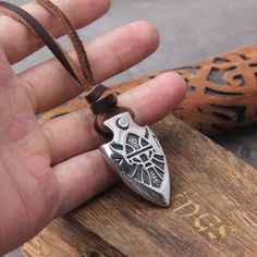 a hand holding a silver pendant on a brown leather cord with an ornate design in the middle