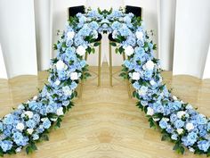 blue and white flowers are arranged in the shape of an arch on a wooden floor