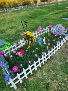 a white picket fence with fake flowers in the grass and an umbrella on top of it