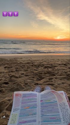 an open book sitting on top of a sandy beach next to the ocean at sunset