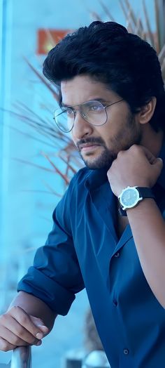 a man with glasses is leaning on a railing and looking at the camera while wearing a blue shirt