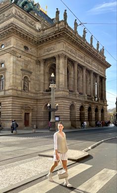 a woman walking across a cross walk in front of a large building