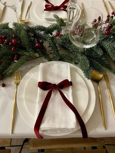 the table is set with white plates, silverware and greenery for christmas dinner