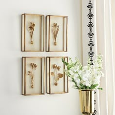 three gold framed flowers on a wall next to a vase with white flowers in it