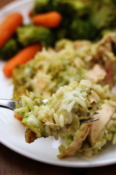 a white plate topped with broccoli and rice covered in sauce next to carrots