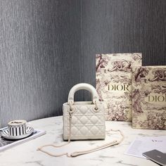 Features: Latte Cannage Lambskin Reference: M0505ONGE_M030 The Lady Dior handbag epitomizes the House’s vision of elegance and beauty. Refined and sleek, the timeless creation is crafted in latte lambskin and covered with Cannage stitching, creating an instantly recognizable quilted texture. The pale gold-finish metal D.I.O.R. charms embellish and illuminate its silhouette. Featuring a removable chain shoulder strap, the miniature Lady Dior bag can be carried by hand or crossbody as an ideal evening wear companion. Removable chain Interior zip pocket The bag may be paired with different embroidered straps Dust bag included Dimensions: 17 x 15 x 7 cm / 6.5 x 6 x 3 inches The size is ideal for a Lotus wallet or an iPhone 13 Pro Max, as well as lipstick Mini Lady Dior, Lady Dior Handbag, Signature Quilts, Kitty Meow, Dior Handbags, Pale Gold, The Lady, Lady Dior Bag, Classic Flap