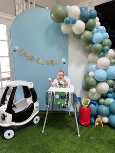 a baby sitting in a crib next to a balloon arch with the words, we're in one