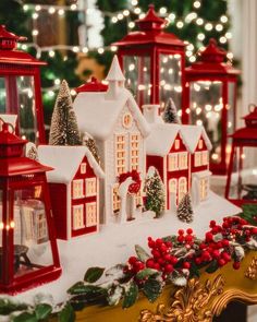 a christmas scene with red and white lit up houses in the snow, surrounded by holiday decorations