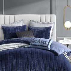 a bed with blue comforter and pillows in a gray room next to a white table