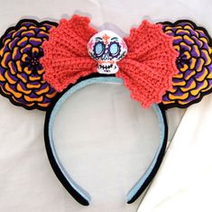 a crocheted mickey mouse ears headband with a skull in the middle and a red bow at the top