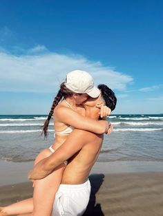 two women hug on the beach while wearing white bathing suits