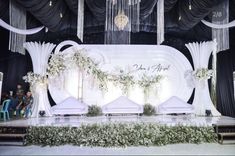 a stage set up for a wedding ceremony with white flowers and greenery on it