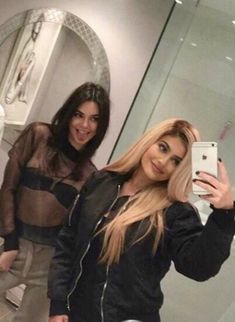 two beautiful young women taking a selfie in front of a bathroom mirror with their cell phone