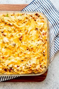 a casserole dish with chicken and cheese in it on a wooden tray next to a blue striped napkin