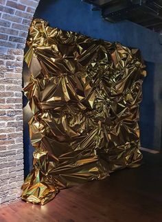 a large piece of gold foil sitting on top of a wooden floor next to a brick wall