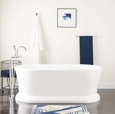 a white bath tub sitting on top of a wooden floor next to a blue rug