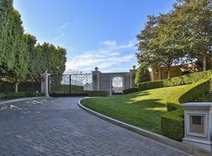 the driveway is lined with trimmed hedges and stone walkways that lead to an iron gate