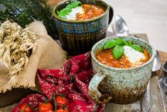 two mugs filled with tomato soup and garnished with fresh basil, tomatoes and sour cream