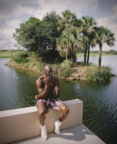 a man sitting on a wall next to a lake talking on a cell phone with palm trees in the background