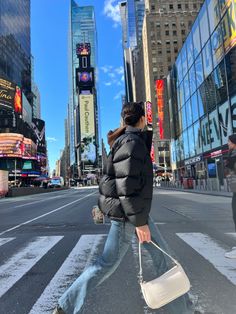 a man walking across a cross walk in the middle of a busy city with tall buildings