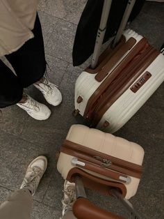 two people standing next to each other with suitcases on the ground in front of them