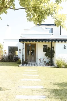 a white house with a black roof and door on the grass area in front of it