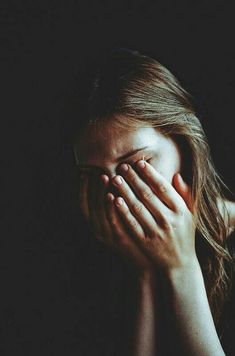 a woman covering her face with both hands in front of her face, against a dark background