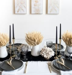 the table is set with black and white plates, silverware, wheat stalks, and candlesticks