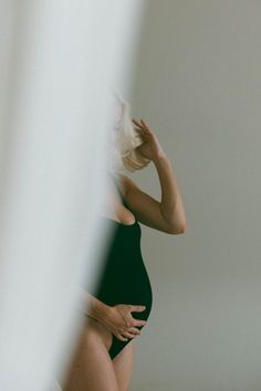 a woman in a black bodysuit is looking at her cell phone while leaning against the wall