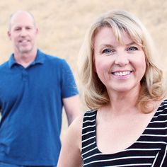 a man and woman standing next to each other in front of a field with grass