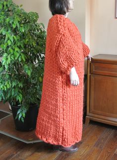 a woman standing in front of a potted plant wearing an orange knitted sweater