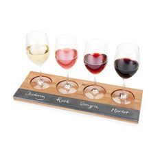 four glasses of wine sitting on top of a wooden board with the names of different wines