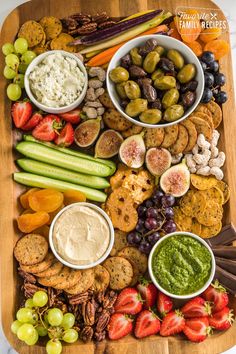 a wooden platter filled with crackers, dips, fruit and veggies