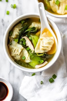 two bowls filled with dumplings and vegetables next to dipping sauce on a white towel