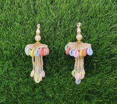 two pairs of earrings with beads and pearls on them sitting in the middle of some grass