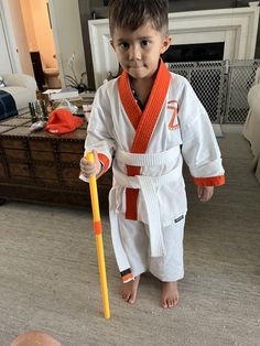 a young boy holding a yellow stick and wearing a white kimono standing in a living room