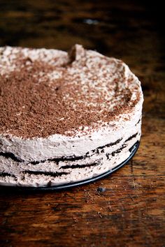 a cake with white frosting and chocolate sprinkles on it sitting on a wooden table